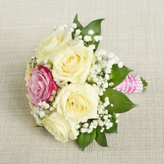 Gracefully displayed on a softly textured neutral fabric, this compact bridesmaid's bouquet exudes the understated style associated with Clerkenwell's heritage. Its centrepiece is a cluster of five or six creamy, latte-hued roses, their tightly swirled petals hinting at new beginnings and fresh promise. Just offset, a striking fuchsia-pink rose commands attention, its intensity contrasting dramatically with the paler blooms around it-like a burst of colour on a Clerkenwell morning. Clusters of cloud-like white gypsophila weave throughout, adding an ethereal softness and balancing the boldness of the magenta rose. Deep green, glossy leaves peek from beneath, their natural sheen evoking the freshness of leafy corners near Clerkenwell Green and the tranquil edges of local gardens. The arrangement's stems are wrapped in vivid fuchsia satin ribbon, carefully wound with luminous white pearls, each turn reflecting a quiet sophistication often seen in the area's boutique events. The gently diffused light accentuates every curve and detail, while the blended scents of fresh roses and greenery evoke moments of joy and anticipation. Whether destined for a fashionable wedding ceremony along St John Street or a special celebration at a nearby venue, this bouquet embodies the artistic vibrancy and subtle luxury for which Clerkenwell is known.