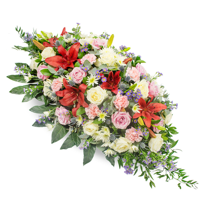 Set against a pristine white background, a large, double-ended casket spray stretches in a gentle diagonal arc, rich with colour and texture yet composed with calm restraint. The eye is first drawn to the dramatic red lilies, their broad, star-shaped petals opening fully to reveal intricate markings and deep, velvety tones. These strong blooms are surrounded by layers of roses in white, cream, and delicate pink, some just beginning to open, others fully unfurled, creating a sense of time passing and a life remembered through many stages. Pale pink carnations with finely ruffled petals and white, multi-headed spray chrysanthemums fill out the heart of the design, making the arrangement feel full and generous. Threaded through this soft tapestry are subtle accents of purple and blue: spiky thistle-like flowers with silvery-blue heads, and airy tufts of lavender or statice that bring depth and a gentle coolness to the palette. All of this rests on a substantial bed of dark green foliage, including broad, glossy leaves and lighter, feathery greens that extend a little further at each end, emphasizing the elongated shape typical of a casket tribute. The design feels considered and balanced, the work of a florist who understands both classical funeral traditions and the quieter, modern tastes of families in Clerkenwell. You can almost imagine this spray being carried carefully through one of the area's old churches or civic buildings, a floral expression of respect, sympathy, and enduring love for a final farewell.