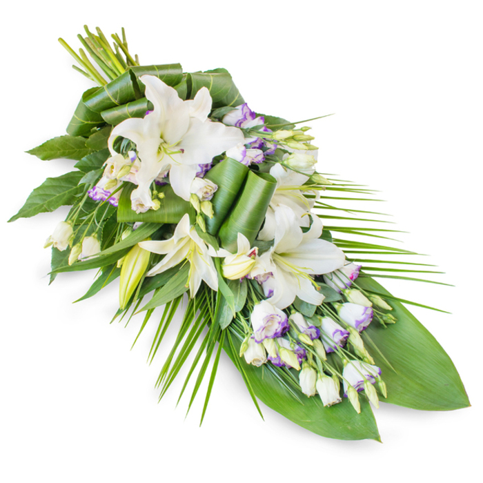 This image shows a dignified, teardrop-shaped funeral spray arranged in a diagonal line, resting visually from the top left to the lower right against a clean white background. The focal flowers are generous white lilies, many of them fully open with wide, arching petals and soft green throats framing delicate stamens dusted in pale pollen. They give the impression of calm, steady light. Interspersed among these larger blooms are stems of lisianthus, whose smaller, cup-like flowers create a fine lacework of detail. Most of the lisianthus are white, yet several petals are edged with gentle lavender and pale purple tones, reminiscent of the soft colours that settle over Clerkenwell's historic rooftops at the end of the day. Tight lisianthus buds stand upright, adding height and a sense of continuing life to the composition. The entire spray is supported by a carefully constructed base of foliage. Larger, deep green leaves lie broad and protective beneath the flowers, some of them subtly glossy, reflecting just enough light to emphasise their rich texture. Higher up, selected leaves have been meticulously curled and looped into elegant, modern shapes, showing the skilled hand of a professional florist from Clerkenwell Flowers. Toward the right edge, long, narrow palm-like fronds sweep outward and downward, echoing the graceful arc of the design and suggesting a gentle bow or final nod of respect. The colour story of white, green, and touches of lavender conveys purity, peace, and remembrance, making this spray ideal for a casket, chapel, or memorial table in and around Clerkenwell, from Rosebery Avenue to the quiet side streets near St John's Gate.