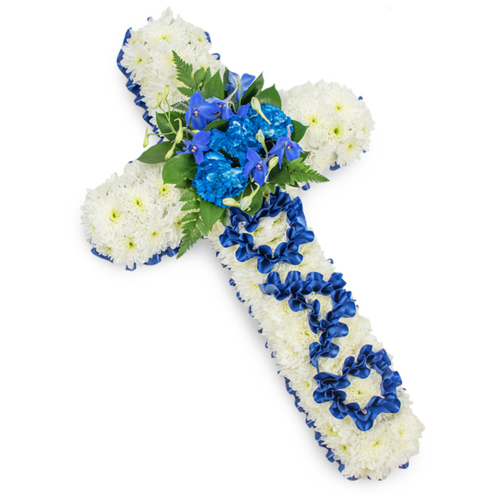 A meticulously crafted floral cross, created as a sympathy tribute for a father, is photographed from above on a bright, seamless white background, highlighting every detail of the design. The cross is fully covered with masses of small, pristine white spray chrysanthemums, their tightly packed petals forming a cushioned, almost quilted surface that looks both soft and substantial. Around the entire outline of the cross runs a rich royal-blue satin ribbon, neatly pleated and turned at the corners, giving a clean, defined silhouette and introducing a note of solemn elegance that would sit beautifully in a service at a Clerkenwell church or crematorium chapel. At the point where the arms meet the upright, a generous cluster of vivid blue flowers becomes the central feature: luxuriant blue carnations with ruffled, layered petals, combined with upright florets resembling blue delphiniums or orchids. These blue blooms are framed by feathery dark-green ferns and smooth, deeper green leaves, which add contrast and a natural, garden-like feel amidst the structured form. Running down the vertical stem of the cross, the word DAD is delicately spelled out using the same royal-blue ribbon, its loops and folds carefully shaped into clear, legible letters that sit proudly against the white cushion of chrysanthemums. The lighting is even and soft, casting only the faintest shadow and allowing the viewer to appreciate the different textures: satin ribbon, velvety petals, and airy foliage. The arrangement conveys a profound sense of respect, love, and remembrance, an ideal funeral flower tribute for a cherished father from a local Clerkenwell family wishing to express their final farewell with grace and tenderness.
