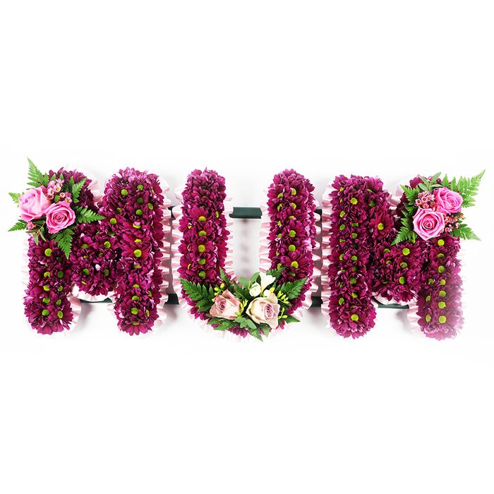 This photograph shows an elegant, three-dimensional MUM floral tribute, likely created by a skilled Clerkenwell florist for a funeral or memorial service. The letters are large, solid, and freestanding, positioned against a simple white background that allows every detail to be clearly seen. Each letter is completely blanketed in tightly arranged spray chrysanthemums in rich fuchsia-purple and deep magenta, the petals forming a continuous, textured surface. Subtle lime-green centres peek from within, giving a natural, fresh contrast against the darker petals. The sides of all three letters are trimmed with a delicate, pale pink ruffled ribbon, carefully pleated to follow each angle and curve, adding an extra touch of softness and hand-finished care. On the first M, the upper left arm carries a small, but striking floral spray: two fully open soft pink roses with several buds in different stages of opening, framed by fine green fern fronds. The central U features a more rounded embellishment resting at its base, a mix of lighter blush roses and creamy white blooms, reminiscent of freesia, arranged with more fern leaves to create a gentle cradle within the letter's bottom curve. On the final M, the top right arm holds a complementary cluster of vibrant pink roses and fern foliage, visually balancing the first spray. The composition feels calm and reverent, the magenta tones offering strength while the pastel roses provide comfort. It is the kind of bespoke tribute one might see travelling from a studio near Exmouth Market to a quiet farewell at a local Clerkenwell crematorium, expressing deep love and gratitude to a cherished mother.