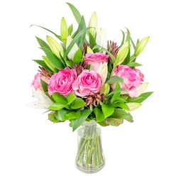 A refined bouquet sits in a simple clear glass vase, the composition centred on richly hued pink roses and poised white lily buds, set against a clean white background so every detail reads clearly. The roses dominate with full, unfurled heads in deep fuchsia and softer blush shades, their velvety petals catching the light and offering a sense of warmth and romance. Around them, tall white lilies alternate between tight, elegant buds and those just beginning to open, their pale throats and slender stamens promising the soft, heady scent of lilies. Lush greenery - a mix of glossy broad leaves and delicate, airy sprigs - forms a verdant frame that amplifies the colours and adds sculptural volume. Specks of darker burgundy or reddish-brown accent foliage are woven through the arrangement, introducing contrast and a subtle, rustic edge. The vase's tapered profile reveals clear water and neatly aligned stems beneath, an honest detail that speaks to freshness and care. Speaking as a local florist, this is the kind of bouquet we'd recommend for a Chelsea flat or a quiet Clerkenwell office near St John Street; it's both striking as a centrepiece and intimate as a bedside surprise. Available for local delivery across Clerkenwell and nearby Farringdon, this arrangement - prepared in our workshop at Clerkenwell Flowers - communicates celebration, gratitude and elegant sympathy with a restrained, hand-crafted sensibility.