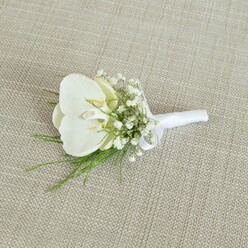 A delicately crafted white orchid boutonniere lies on a neutral, light tan fabric with a visible woven texture, similar to softly worn linen or fine burlap you might see in a Clerkenwell interiors shop. The focal point is a single, immaculate Phalaenopsis orchid, its petals broad, smooth, and gently curved, forming a serene white cup that draws the eye inward. At the centre of the bloom, a whisper of pale yellow in the orchid's throat adds depth and a gentle hint of warmth, like early sunlight over nearby Spa Fields. Encircling this central flower are airy sprays of baby's breath, each tiny white blossom forming part of a delicate cloud that softens the boutonniere's outline and introduces a sense of romance. Threaded between the gypsophila are fine strands of vibrant green foliage, slender and feathery, which provide subtle texture and a fresh, garden-like feel, as if the greenery had just been gathered from a leafy corner near Clerkenwell Green. The stems of the orchid, baby's breath, and foliage are tightly bound together with a smooth white satin ribbon, wrapped with precision and finished in a small, neat bow that rests close to the base of the design. The ribbon's clean, bright surface contrasts elegantly against the natural fibres of the background fabric. Soft, even lighting reveals the gentle shadows cast by each petal and sprig, giving the image a quiet, contemplative mood. This refined floral accessory feels perfectly suited to a contemporary London wedding, an intimate civil ceremony, or a stylish event, capturing the understated elegance and thoughtful detail that a local Clerkenwell florist would bring to a groom's or groomsman's lapel.