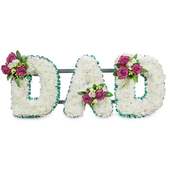 This image shows a carefully crafted sympathy lettering piece that reads DAD in large, three-dimensional letters, each constructed from a tight, velvety mass of white chrysanthemums that produce a soft, serene texture across the surface. The letters are set on a clean white background, which lets the pristine white blooms appear almost luminous under gentle studio light. Each letter's perimeter is bordered with a ruffled emerald-green ribbon, the pleated edge creating a cool contrast that sharpens the letterforms and lends an understated formality suited to a memorial setting. Positioned with deliberate care, three small clusters of rich magenta roses add a warm, personal note: the first cluster rests on the upper left curve of the first D, the second nestles within the lower V of the A, and the third graces the upper right curve of the final D. Interspersed among the roses are tiny white freesia-style flowers and deep green foliage, which add lightness, scent and depth to the composition. A slim, dark green support bar behind the letters suggests the arrangement is freestanding for display at a funeral service or graveside. The overall impression combines traditional dignity and hands-on craftsmanship-a floral conversation that says love, respect and farewell. As a Clerkenwell-based florist familiar with local church halls and funeral lodges around St John's Square and Cowcross Street, I picture this tribute arriving warmed by familiarity and crafted for a father deeply cherished.