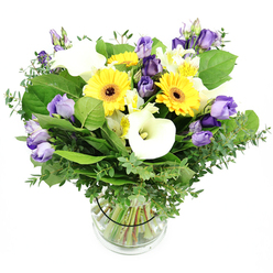 There's something utterly uplifting about this design, a sunlit harmony that draws you in with effortless contrast yet feels entirely cohesive. The bright yellow Gerbera daisies bloom like little suns, their centers a rich, grounding brown that anchors the bouquet, while pristine white Calla lilies rise with smooth, sleek elegance. Between them, clusters of ruffled Lisianthus drift in lavender to deep purple, some fully open and others still as poised buds, creating a soft, architectural depth. A generous chorus of greenery-glossy leaves, slender eucalyptus with its silvery tint, and wisps of finer foliage-gives the arrangement both fullness and fragrance, the scent subtle and fresh in the air. In a clear vase, the stems are arranged with a relaxed, natural grace, the water catching the light and revealing a clean, orderly cross-section that speaks to the care of a skilled florist. As I imagine this bouquet arriving at a doorstep, I picture it brightening a Clerkenwell flat near Exmouth Market or along King's Cross Street, perhaps for a milestone or simply to lift a day. Clerkenwell Flowers can arrange same-day delivery across Clerkenwell and nearby neighbourhoods, ensuring the moment of opening the door is met with sunshine. It's the kind of bouquet that feels appropriate for birthdays, anniversaries, or a thoughtful gesture to a dear friend in Islington or the Barbican area, radiating warmth, optimism, and modern elegance.
