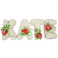 This elegant memorial arrangement spells KATE in large, raised letters formed from a dense, even carpet of white chrysanthemums, each tiny bloom layered to create a soft, cloud-like texture that conveys peace and reverence. A frilled pale-pink ribbon edges each letter, introducing a gentle, human touch that contrasts the cool white surface. Strategic clusters of red anthurium blossoms, with their glossy, heart-shaped spathes and central spadices, are nestled into the white base to provide warm, heartfelt focal points; surrounding them, deep green foliage - glossy broad leaves, delicate fern fronds and fine trailing vines - is woven through the letters to add depth, movement and a sense of living connection between the characters. The whole composition sits against a bright white background with a faint drop shadow beneath, which lifts the letters visually and makes the tribute read clearly from a distance. The scent is subtle, a faint green and floral note from the chrysanthemums and foliage rather than anything overpowering, appropriate for a chapel setting, funeral service or celebration of life. As a Clerkenwell florist familiar with services at nearby St John's Gate and gatherings around Smithfield, we place a premium on balance and legibility so the name remains the heartfelt centre of attention. This bespoke design, prepared with careful selection of long-lasting chrysanthemums and hardy anthuriums, is meant to offer comfort and a dignified final farewell.
