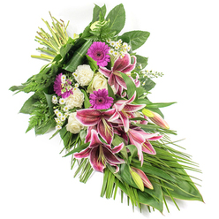 A refined sympathy sheaf is displayed on a crisp white background, its form sweeping gently from top left to bottom right, echoing the curve of a teardrop and conveying a soft sense of farewell. At its heart, dramatic Stargazer lilies open wide, their petals a saturated fuchsia-pink with snowy white edges and dark burgundy freckles, glowing as if in soft chapel light. Some lily buds remain closed, with tips flushed in pink and green, hinting at life and beauty still to come. Beside them, bright magenta gerbera daisies introduce a burst of optimism and fond recollection, while creamy white roses and ruffled white carnations nestle close, bringing serenity and tenderness. Delicate white daisies and tiny filler blooms weave between the larger flowers, adding a lace-like texture that softens the arrangement. The flowers are cradled in generous green foliage: broad, deep green leaves provide structure, feathery fern fronds create a gentle halo, and long, sleek leaves arc outward and downward, emphasizing the elongated, cascading line. At the top left, the stems are tightly bound, revealing a hand-crafted design created with care, much like the thoughtful tributes prepared for services near Clerkenwell Green or St John Street. The composition feels both solemn and quietly hopeful, suitable for a funeral, memorial, or cremation service, and it reflects the calm dignity that families in Clerkenwell often seek when saying goodbye to a loved one.