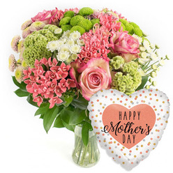 Set against a bright white backdrop, this Mother's Day gift ensemble feels like a moment of calm celebration captured in a studio just off Clerkenwell Road. A rounded bouquet overflows from a clear glass vase, its stems neatly gathered and immersed in clear water, suggesting freshness and careful local preparation. At the centre, full pink roses with softly ruffled petals provide a romantic focal point, their blush tones deepening slightly toward the edges. Around them, tight clusters of coral-pink flowers, similar to kalanchoe, form dense pockets of colour that echo the warmth of a spring morning walk through Spa Fields. Lime-green button chrysanthemums and velvety, frilled green florets bring a lively, modern twist, their vivid hues and textured forms giving the design a playful yet refined character. White daisy-like spray chrysanthemums and tiny multi-petalled blooms with pale pink or yellow-tinted centres add brightness and a gentle airiness, as if light is filtering gently through them. Dark green foliage frames the composition, grounding the pastel and citrus tones with natural depth. Just to the right of the vase, a gleaming heart-shaped foil balloon adds a festive finishing note. Its white or soft silver surface is scattered with irregular gold, silver, and peach polka dots, drawing the eye inward to a bold peach-coloured heart stamped with the words HAPPY Mother's DAY in a mix of bold and script black fonts. The image captures the feeling of a carefully curated Mother's Day bouquet and balloon, the kind Clerkenwell Flowers might send for same-day delivery to homes and studios around Farringdon, Barbican, or Sadler's Wells, combining heartfelt sentiment with fresh floral artistry.