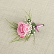 A romantic pink rose boutonniere is carefully displayed against a pale beige, linen-like fabric that feels very much in keeping with Clerkenwell's mix of old brick workshops and modern studios. The rose itself sits on a slight diagonal, occupying the lower left of the scene, its petals layered in soft curves. Deeper magenta edges fade into a gentle pastel pink as they move inward, creating a subtle gradient that suggests tenderness and new beginnings. Surrounding the bloom, dainty clusters of white baby's breath hover like tiny stars, their airy nature giving the design a light, almost whispery presence. Wispy green blades of foliage extend beyond the rose, adding height and movement, while a single wider green leaf has been artfully wrapped at the base, cradling the stem and catching a few jewelled droplets of water that shimmer in the light. The stems are tightly wrapped in satin ribbon, a muted blush pink that feels smooth and cool to the touch, secured with a slightly darker pink bow that adds a refined finishing touch without overpowering the flower. The overall palette is soft yet confident, suitable for a groom or prom guest walking through Clerkenwell's cobbled lanes toward a celebration. This boutonniere speaks of considered design and local florist expertise, the kind of piece chosen with care at Clerkenwell Flowers for an intimate wedding, a civil ceremony near Exmouth Market, or a special evening where one elegant rose can carry a whole story.
