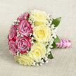 A beautifully composed hand-tied bouquet lies on a pale, woven fabric that looks like natural linen, its understated beige tones setting off the colours of the flowers. Viewed from above, the bouquet has a perfectly rounded shape, almost like a floral mandala, with half the circle formed from plush fuchsia and magenta-pink roses and the other half from softly glowing, creamy yellow roses. Each rose is at its peak, petals unfurling in tight, elegant spirals that suggest both luxury and tenderness. Threaded between the roses are fine clusters of white gypsophila, or baby's breath, creating a light, cloud-like veil that softens the edges and adds a romantic, traditional touch. A few deep green leaves anchor the design, hinting at the freshness of flowers that might have come straight from a London flower market up the road from Clerkenwell. The stems are gathered into a compact handle, smoothly wrapped in lustrous pink satin ribbon and decorated with a delicate winding of tiny white pearls, echoing a string of bridal jewellery. The light in the image is gentle and diffuse, so the pinks, yellows, and whites appear calm and soothing rather than bright or harsh, like a quiet morning before a wedding ceremony in one of Clerkenwell's converted warehouses. You can almost imagine the subtle, sweet fragrance of the roses and the way the bouquet would feel cradled in the hands-cool ribbon, smooth pearls, and the reassuring weight of fresh blooms, perfect for a wedding, vow renewal, or intimate celebration in the heart of EC1.