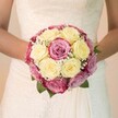 There's a quiet intimacy to this wedding bouquet, lovingly crafted by a Clerkenwell florist to cradle a story of romance in every bloom. The rounded arrangement, held gently at waist-height by the bride, is a poetic trio of creamy yellow roses, fuchsia pink roses, and softly blushed petals that drift into subtle mauve-a painterly palette that feels both modern and timeless. Wisps of gypsophila, with their fleecy white blossoms, spill among the roses, giving the bouquet an airy lightness, while the deep green leaves tucked beneath echo the vibrant greenery found in the parks and hidden courtyards of Clerkenwell. The bride's gown, glimpsed in close-up, features a bodice of delicate lace-a swirl of craftsmanship and tradition-before flowing into a pristine, smooth skirt. Bright, even lighting caresses every surface, illuminating the bouquet's fresh textures and capturing the anticipation woven into each petal. Behind, the background softly blurs away, ensuring nothing distracts from the artistry at hand. This image captures more than beautiful flowers: it distills Clerkenwell's unique blend of history and creative celebration into one unforgettable bridal moment, ideal for sharing stories of local weddings, florist talent, and cherished beginnings.