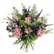 Set against a bright white background, this abundant bouquet feels like a breath of colour carried in from a quiet walk through Clerkenwell on a spring morning. The flowers are arranged in a generous, rounded shape, every angle revealing another layer of soft pink and purple detail. Nestled at the centre, pastel pink roses open in smooth, spiralling petals, some still cup-shaped with promise, others more fully unfurled so that you can almost sense their delicate fragrance. Around them, ruffled carnations in dusty rose and mauve add a romantic, cloud-like fullness, their crimped edges catching the light and creating gentle shadows. Rising through this softness, slender spires of deep violet-blue Veronica introduce elegant vertical lines, reminiscent of the tall brick facades along nearby St John Street. Between the spikes, clusters of rich purple lisianthus curl into bell-shaped blooms, their velvety texture offering a deeper, moodier note. Sprinkled throughout are tiny aster-like flowers in lavender and periwinkle, each with a small yellow centre that brings a subtle sparkle and airiness. The bouquet is framed by a lively mix of greenery: bright chartreuse filler and feathery leaves bring a fresh, energetic lift, while cool eucalyptus and other foliage add calming, silvery tones. At the base, the clean, neatly bound stems reveal the hand-tied craftsmanship, ready for a vase on a Clerkenwell desk, a studio near Exmouth Market, or a dining table shared with friends. This arrangement conveys gentle celebration and affection, ideal for marking meaningful moments, from birthdays and anniversaries to a simple thank-you delivered the same day to someone special in EC1.
