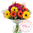 A beautifully lit studio scene showcases a ready-to-gift floral arrangement designed for a special mum, composed of a vibrant bouquet of Gerbera daisies paired with a charming balloon. The bouquet forms a rounded canopy of colour, with large daisy-like blooms in bright yellow, glowing orange, and intense magenta, each flower open to its fullest, revealing the distinctive dark central disk. The petals spread out in flawless, even layers, creating a sense of symmetry and radiance, as though the arrangement is quietly glowing in a Clerkenwell townhouse near Farringdon Road. Between the colourful heads, dark green leaves and foliage peek through, giving the composition depth and a natural, freshly picked character. The stems are gathered together and wrapped in a soft, rustic sheet of light brown kraft paper, its mildly crumpled surface adding texture. Over this lies a transparent layer of shiny cellophane that hugs the bouquet, catching highlights and emphasising the flowers' brightness. A length of natural-coloured twine is tied neatly around the wrapping, forming a simple bow that suggests an attentive, hand-made touch from a local florist. The entire bouquet stands in a clear glass vase filled with water, allowing the viewer to see the straight green stems aligned in an orderly fashion. To the lower right of the flowers, a single round white foil balloon brings a festive accent. The balloon is sprinkled with metallic gold and pink confetti-style dots and tiny hearts that seem to float across its surface. At its centre, the phrase best Mum is written in flowing pink script, making the purpose of the gift unmistakable. Together, the vivid gerberas and celebratory balloon evoke joy, gratitude, and warm family affection, perfect for a Mother's Day surprise or a heartfelt thank-you in Clerkenwell.