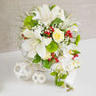 An opulent wedding centerpiece sits poised on a white tabletop, the kind of refined bouquet you might imagine gracing a reception in one of Clerkenwell's converted loft venues. Dominated by crisp white Oriental lilies, the arrangement is full and generous, each lily unfurling its broad, velvety petals to reveal soft speckles and long, pollen-tipped stamens that lend a sense of living movement. At the heart of the design, a single yellow rose swirls into a perfect spiral, its creamy, sunlit petals glowing with warmth against the cooler whites and greens, like a small patch of sunshine filtering through the tall windows of a Clerkenwell townhouse. Clouds of white baby's breath are nestled between the larger blooms, their tiny blossoms adding a misty, romantic veil, while vivid, spherical Green Trick dianthus create a playful moss-like contrast that feels unexpectedly modern. Fine, feathery foliage in fresh herb greens threads through the composition, softening every edge and giving the bouquet an organic flow, as though gathered from an elegant urban garden. Glossy red hypericum berries punctuate the design, their garnet-like shine adding festive energy and a hint of winter cheer without overpowering the sophisticated palette. To one side, a cascading trail of white Phalaenopsis orchid blooms sweeps gracefully downward, each orchid immaculate and gently curved, with tender green buds and slender, spiky accents adding rhythm and anticipation. All of this is supported by a white woven basket base, its subtle pattern echoed in two decorative white spheres resting nearby, tying the scene together. The overall effect is one of quietly confident luxury, perfect for a contemporary Clerkenwell wedding table or a special anniversary dinner at home, where every petal and texture tells a story of care and artistry.