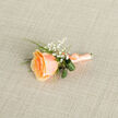 Presented as if laid down after a brief pause on a walk from Leather Lane to Farringdon, this buttonhole arrangement centres on a single apricot-rose bloom whose petals curl inward in delicate spirals. The rose's colour moves like a soft sunset across the petals - deeper apricot at the core, melting to peach and pale cream at the edges - and its velvety surface invites a gentle fingertip. Around this heart, clusters of tiny white gypsophila scatter visual light, their fine sprays creating an impression of ephemeral snowfall against the rose's warmth. Two darker green leaves are artfully rolled and tucked behind the bloom, providing sculpted contrast, while slim, bright-green grass blades weave through the grouping to add a lively vertical thread. The stems are bound with a coordinating peach satin ribbon, finished into a small bow that gleams faintly under neutral studio light; a small metallic pin or wire is visible at the base, practical and unobtrusive, ready to secure the buttonhole to a lapel. The bouquet reclines on a light beige, woven linen backdrop whose cross-hatch texture complements the composition's handcrafted restraint. There is a quiet romance here - the scent of fresh rose and a trace of green - and it feels distinctly local: the kind of boutonniere guests might wear to a wedding near St John's Street or a summer celebration in Clerkenwell's tucked-away courtyards.