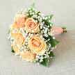 Arranged with the care of a neighbourhood florist, this bridal bouquet centres on soft peach roses gathered into a compact, luminous cluster, their creamy faces opening like small suns. Around them, a froth of white gypsophila forms an ethereal cloud that softens edges and adds a sense of innocent wonder; each tiny star-shaped bloom refracts the light and contrasts the roses' satiny surfaces. Sprigs of glossy greenery-deep emerald leaves with a subtle sheen-peek through and provide both contrast and lift, shaping the bouquet's rounded form so it feels balanced and easy to carry down narrow Clerkenwell streets toward Farringdon. The handle is wrapped in peach satin ribbon, the fabric pulled taught and finished with a neat row of pearls that glimmer with every tilt, offering a nod to tradition and a tactile comfort for a bride's hand. The scent is gentle and refined: the roses' soft fragrance warmed by sunlight, brightened by the clean, green whisper of foliage. As a local florist who prepares wedding flowers for ceremonies near Exmouth Market and small receptions around Charterhouse Square, I imagine this arrangement calming nerves and catching photographs in soft window light. Prepared with fresh, hand-selected stems and designed to sit lightly in the hand, the bouquet feels like a small, hopeful ritual-perfect for a bride seeking classic elegance with a modern, Clerkenwell touch, and available for collection or local delivery within the area from Clerkenwell Flowers.