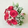 Lying gracefully on a softly textured, cream-hued fabric-like those found in the welcoming cafes of Clerkenwell-this hand-tied bouquet brings together classic beauty with contemporary flair. Prominent red roses rest at the centre, their petals unfurling in perfect spirals, each bloom displaying a lush, velvety crimson that captures the romance of a summer evening in Spa Fields. Delicate clusters of white baby's breath fringe the roses, their cloud-like softness adding a sense of airiness and gentle innocence that elevates the arrangement's overall charm. Hints of deep green foliage-perhaps ruscus or salal-are tucked between the petals, their glossy sheen reminiscent of the vibrant plant life scattered around St John's Gardens. The bouquet's stems are secured with a bold, red and white striped ribbon, finished with an elegant twist of petite pearls, highlighting the skillful hands of Clerkenwell's expert florists. Soft daylight bathes the composition, emphasizing each petal and bead, inviting thoughts of joyous weddings, anniversary gatherings, or heartfelt thank-you gestures shared beneath Clerkenwell's leafy canopies. The bouquet's gentle fragrance whispers of fresh roses and spring greens, making this image an inspiring choice for those seeking meaningful floral arrangements for life's most treasured milestones in the heart of London.