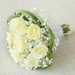 There's a quiet poetry in this bouquet-an interplay of creamy white roses opening like whispered promises, their soft fragrance blending with the delicate, powdery scent of abundant gypsophila. The image evokes a sense of cool early light over Clerkenwell, where classic romance meets modern sensibilities. Wisps of baby's breath encircle each rose, their airiness as gentle as a morning breeze from St James's Church garden. Dynamic loops of glossy green bear grass lend a whimsical edge, framing the floral heart with lively arcs that echo Clerkenwell's creative energy. Bound with a smooth silver ribbon adorned with rows of tiny lustrous pearls, the handle gleams subtly, inviting a tender touch. Slightly exposed, the green stems peek from their pearly band, grounding the bouquet in authenticity and London freshness. This floral design, ideal for weddings or heartfelt gatherings throughout Clerkenwell and Farringdon, speaks of new beginnings, enduring love, and the artisan skill of local florists. Every detail-colour, texture, and form-contributes to a lasting impression of serene celebration and refined beauty.