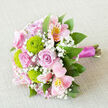 Captured from above on a pale, softly woven cloth that looks like natural linen, this hand-tied bouquet feels like a quiet moment of celebration in the middle of Clerkenwell. At its centre, full-headed pink roses unfurl in gentle spirals, their petals layered and velvety, suggesting romance without being overly formal. Nestled closely among them, lime-green button chrysanthemums form small, rounded bursts of colour, their textured petals giving the arrangement a crisp and contemporary edge. Pale pink alstroemeria arch outward, each bloom etched with fine maroon streaks and warm yellow flashes at the throat, adding a touch of exotic refinement. Wisps of baby's breath drift between the larger flowers, their tiny white blossoms creating a soft, clouded veil that breaks up the colour and adds a sense of lightness and breath. Cool green foliage surrounds and supports the central blooms, the leaves slightly glossy and layered so that the bouquet appears full yet well balanced, like something freshly gathered from a city garden off Clerkenwell Green. The stems are carefully straightened and bound with a smooth, satin ribbon in deep fuchsia, which wraps around the handle in neat, secure coils, leaving the cut ends visible at the base. The lighting is even and gentle, catching the satin's sheen and the natural curves of each petal without creating harsh shadows. It is the kind of bouquet a local florist near Farringdon Station might prepare for a small wedding, an anniversary dinner on St John Street, or a same-day delivery surprise to a studio apartment overlooking the historic squares of EC1.