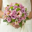 In the gentle light of a Clerkenwell morning, a bride's hands hold a bouquet that seems to float with delicate promise. Whisper-soft pink and lavender roses swirl at the center, their subtle scent hinting at celebration and new beginnings, reminiscent of nuptials near St John's Square or a joyful gathering in Amwell Street's historic halls. The roses' silky petals are contrasted by vivacious lime green button chrysanthemums, whose rounded forms bring a breezy energy and a cheerful, contemporary flair to the arrangement. Woven throughout, sprays of white baby's breath give the bouquet an airy innocence-like a soft sigh or the laughter rising from a wedding party in nearby Spa Fields. Pink alstroemeria with maroon-flecked petals glimmer delicately, each bloom whispering stories of romantic adventure and heartfelt union. Glossy dark green leaves cradle the symphony of flowers, adding depth and grounding the playful palette. The bouquet's soft glow and intricate design embody both serenity and joyful momentum-a piece artfully fashioned by a local Clerkenwell florist for a radiant wedding day filled with hope, connection, and understated luxury.