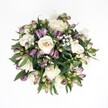 Top-down view of a hand-tied, circular bouquet set against a crisp white background, where every bloom seems to float in quiet balance. At the heart of the arrangement are generous creamy white roses, their petals unfolding in soft spirals from warm ivory to pale champagne, each flower at a slightly different stage of opening. Nestled closely around them are slender buds of purple alstroemeria, the Peruvian lilies still mostly closed, tipped with deep lavender and rich plum that fade into fresh green at the base. Between these larger forms, clouds of tiny white gypsophila dot the design like a fine mist, giving the bouquet an airy, almost weightless quality. Dark green foliage with a subtle sheen forms a relaxed ring beneath the flowers, leaves curving gently outward and peeking through the blooms to create depth and natural movement. The light falling over the bouquet is soft and even, as if caught near a bright Clerkenwell studio window, without harsh shadows, allowing each texture to be clearly defined: the velvety rose petals, firmer alstroemeria buds, and feather-light baby's breath. The overall impression is of calm, layered elegance, a modern classic that would feel at home on a quiet kitchen table off Exmouth Market or on a polished office desk near Farringdon. It carries the mood of thoughtful celebration and tender reassurance, ideal for offering comfort, marking an anniversary, or sending gentle congratulations. Though the image is still, the interplay of ivory, purple, and deep green gives the arrangement a living, breathing presence, as if freshly arranged for same-day delivery in Clerkenwell just moments ago.