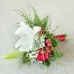 Nestled on a softly textured, light beige linen that evokes Clerkenwell's sophisticated yet inviting vibe, this beautifully arranged floral piece radiates quiet elegance and joyful celebration. The focal point is a magnificent white lily, its open petals spreading outward in a graceful arc, highlighted by subtle russet freckles and golden anthers-suggesting purity and hope. A lush deep red rose sits alongside, its velvety, spiralled petals a symbol of romance and commitment, recalling many special moments shared in Clerkenwell's historic venues. Sprigs of delicate baby's breath add a dreamy, weightless quality, while clusters of red berries bring energetic bursts of colour reminiscent of the lively weekends in Exmouth Market. Alongside, a slender green lily bud reaches forward, hinting at promise and the unfolding of new memories. Diverse green foliage frames the scene-from wispy fern fronds to substantial dark leaves-reflecting the hidden green corners of Clerkenwell. The expertly gathered stems are finished with a smooth, satin red ribbon, tied just so, lending polish and cohesion to the bouquet and mirroring the array's vivid hues. This compact yet artful arrangement combines tradition with modern festivity, perfectly suited for a wedding, anniversary, or special gift destined for any occasion in the heart of Clerkenwell, crafted by local florists who understand both the community's taste and its passion for beauty.