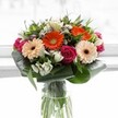 Vivid and full of life, this contemporary bouquet arrives in a sleek glass vase, its composition thoughtfully echoing the creative spirit of Clerkenwell. Dominated by playful gerberas-radiant orange and delicate peach-each bloom unfurls against a backdrop of luminous white, reminiscent of airy studios along Farringdon Road. Tightly coiled magenta roses introduce a thread of passionate sophistication, their colour deepened by the presence of bright, snow-white alstroemeria and airy clusters of tiny blossoms. Lush, glossy aspidistra leaves are meticulously folded, forming a graceful collar that cradles and shapes the arrangement, echoing the leafy parks that dot the neighbourhood. Between flowers, fine sprigs and pointed leaves add natural movement and visual interest, while the transparent vase displays lively green stems in a tangle of fresh vitality-a signature of skilled local floristry. Light pours across the bouquet, bringing a kaleidoscope of warming tones to the fore. There's an uplifting, convivial energy inherent in this display, ideally suited for milestone celebrations, housewarmings, or to lift the mood on a quiet Clerkenwell afternoon. The bouquet radiates warmth, care, and a sense of place, blending artistry and local character in every petal and leaf.