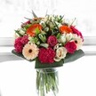 This bouquet, crafted with heart in Clerkenwell, bursts with the spirit of a joyful gathering, frozen in a sunlit moment. Spirited orange gerberas reach outward with warmth, echoing laughter spilling from local cafés near St John's Square. Blush pink roses nestle alongside magenta carnations, their velvety petals soft and rich, while creamy ivory roses and gentle peach gerberas balance the display, lending grace and serenity. Lush, glossy greenery anchors every bloom, its freshness recalling the leafy paths of Spa Fields. The bright, soft light illuminates each petal's gentle veins, causing the bouquet's harmonious colours to truly dance. Whether intended to mark an anniversary in Farringdon or to simply brighten a neighbour's day, this arrangement feels like a burst of seasonal happiness-thoughtfully composed by a florist who knows Clerkenwell's people, rhythm, and style. The bouquet blends expert handwork with local personality, creating a feeling both uplifting and reassuring.