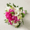 On a soft, sandy-beige linen cloth, a hand-tied bouquet lies as if just set down before a ceremony, radiating gentle excitement. The design centres on lush hot pink peonies, their petals densely layered and slightly frilled, giving the flowers a plush, cushiony appearance that feels almost touchable. Nestled around and between these peonies are bright white alstroemeria, their slim petals curving outwards to reveal throats dusted with fine reddish-brown speckles and faint linear streaks, adding an intricate, painterly detail to the otherwise clean white blooms. Slim green buds with pointed tips pierce the arrangement here and there, offering vertical accents and the sense that some flowers are still waiting to open, capturing a moment midway through spring. Deep green leaves with a smooth, slightly glossy surface peek out from beneath the blossoms, shaping the bouquet into a full, dome-like cluster that gently tapers downwards. Below, a bundle of straight green stems is gathered and wrapped with a satin-finish pink ribbon, wound neatly to form a soft collar at the grip point-practical for a bride walking through Clerkenwell's cobbled side streets or stepping out of a registry office near Farringdon. The overall palette of hot pink, fresh white, and lush green stands out beautifully against the neutral fabric, evoking the feeling of a bright morning before guests arrive. The bouquet suggests romance and gratitude, the type of wedding arrangement often requested from Clerkenwell florists for intimate celebrations, elopements, or simple, heartfelt vows exchanged close to home.