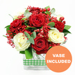 A beautifully balanced bouquet in rich reds and soft creams is shown here, captured against a pure white background that lets the colours breathe. At first glance, the eye is drawn to the full, velvety red roses, each bloom open and layered, radiating warmth and romance. Nestled among them, creamy white roses with gently curling petals bring a serene lightness, the classic combination echoing timeless love stories. Between these larger blooms, clusters of tiny, bright red filler flowers-resembling tinted gypsophila-spread like a fine haze, softening the composition and adding a playful, confetti-like detail. Scattered through the flowers are glossy red hypericum berries, perfectly round and polished, giving a sense of abundance and festive joy, much like the buzz of Clerkenwell cafés and bars on a winter evening. Framing the arrangement, green foliage and rounded eucalyptus leaves create movement, their cool tones and natural texture giving the bouquet a fresh, just-arrived-from-the-market feel. The stems are neatly arranged in a clear, rectangular glass vase, their lines visible through the water, adding a contemporary structure beneath the softness of the petals. A band of green and white gingham ribbon wraps the vase, lending a homey, rustic charm that would look just as fitting on a kitchen table off St John's Square as in a modern office meeting room. In the lower right-hand corner of the image, an orange circular badge with crisp white lettering announces VASE INCLUDED, emphasising that this is a complete, ready-to-display arrangement, ideal as a romantic surprise, a thank-you gift, or a seasonal touch delivered throughout Clerkenwell.