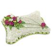 A serene, pillow-shaped sympathy tribute crafted from a dense carpet of pristine white chrysanthemum florets, pictured against a clean white backdrop with a soft shadow beneath that suggests gentle studio light. The cushion surface reads like a cloud-tightly packed, almost velvety petals forming a quietly textured plane that immediately conveys peace and quiet. Along the upper-left corner a compact, luminous cluster of deep magenta roses anchors the design; their velvety petals open with a dignified softness and are threaded through with small, fragrant white freesia or lisianthus blooms that lift the composition with delicate highlights. Fresh green fern fronds and glossy leaves fan out behind the roses, supplying a cool, emerald contrast and natural depth, while two graceful, linear stems of dark green bear grass arc across the white field, drawing the eye from the main cluster toward the opposite corner and creating a simple, flowing movement. Near the lower-right edge a single matching magenta rose rests among a few leaves, balancing the arrangement with a final, contemplative touch. The entire perimeter is finished with a neat, folded lime-green satin ribbon trim, producing a subtle ruffled frame that both defines and softens the silhouette. The overall impression is one of tender craftsmanship and solemn comfort-an arrangement suited to funerals or memorials, evoking restful sleep and reverent remembrance. Imagine this tribute placed at the foot of a chapel pew in Clerkenwell or sent with quiet sympathy to a home near St. Luke's, offering a visual and olfactory calm that supports those grieving without words.