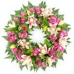 A sumptuous pink and cream funeral wreath is captured in crisp detail against a bright white background, creating the impression of a floating ring of blossoms. The wreath is lavishly packed with roses in shades of deep magenta, vivid fuchsia, and soft petal pink, their textures ranging from tightly wound buds to generous open blooms with many layers of velvety petals. Nestled between them are large, double lilies whose broad petals blend creamy white bases with blush pink and pale peach flushes, some lying wide open like stars, others still encased in slender, pale green buds. The flowers sit on a thick foundation of greenery: dark, glossy leaves and delicate fern fronds that fan outward, their fine leaflets adding a feathery softness around the edges, recalling the natural calm of green corners around Clerkenwell and nearby Islington. The foliage's rich, cool tones answer the warmth of the pink flowers, giving the arrangement both visual balance and a feeling of calm support. The circle is perfect and unbroken, a classic symbol of eternity and unending love, often chosen by families when they want a dignified yet gentle tribute. The composition, free from any visible stand or surroundings, focuses attention solely on the interplay of colour, shape, and texture. It suggests the work of an experienced local florist who understands how to blend sentiment with design, creating a wreath suitable for funerals, church services, crematorium chapels, or private remembrance ceremonies in the Clerkenwell area, where a refined, heartfelt expression of sympathy is desired.