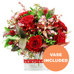 A richly romantic bouquet of red roses and complementary blooms is displayed against a pure white background, its rounded, full silhouette giving the impression of a carefully hand-tied arrangement set down in a modern Clerkenwell apartment near Farringdon Station. At the core, velvety red roses in various stages of opening create a sense of movement and emotion: some buds remain tightly furled, others reveal more of their layered petals, suggesting love that is both tender and intense. These signature roses are interspersed with smaller deep red flowers that resemble alstroemeria or other multi-petalled varieties, their clustered heads adding structure and visual interest without interrupting the unified colour story. Threading between the stronger reds are light, ethereal sprays of tiny pale pink and white filler blooms, reminiscent of waxflower or limonium, which brighten the arrangement and introduce a gentle contrast. A lush halo of mixed greenery surrounds the flowers, from smooth, deep green leaves to finer, more delicate stems that help build a natural, dome-like contour. Punctuating the foliage are distinctive burgundy and russet-toned leaves, some subtly veined, that bring hints of warmth and drama, much like the rich tones found in Clerkenwell's historic brickwork. The bouquet is set in a clear glass vase with a simple rectangular base and softly defined edges, allowing the stems to be seen and giving the composition a clean, contemporary line. Around the vase, a red ribbon patterned with small white hearts is tied neatly, reinforcing the romantic message while staying tasteful and understated. In the bottom right of the image, a circular orange badge bears the words VASE INCLUDED in bold white capitals, making it clear that this is a complete, ready-to-enjoy floral gift, ideal for same-day romantic deliveries around EC1.
