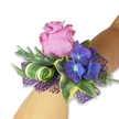 This wrist corsage reads like a small, modern love letter in blooms, designed to sit lightly and confidently on a fair, light-toned forearm. At its heart a single lavender-pink rose unfurls with velvety petals, each layer catching soft light and revealing a faint blush along the edges that suggests both freshness and quiet romance. Nestled close are clusters of deep indigo-blue hydrangea, their tiny florets pooling together like a twilight sky and showing almost-luminous pale blue centers that draw the eye inward. Variegated English ivy frames the composition with glossy, dark-green centers edged in pale cream, adding a classic, romantic border that contrasts with the rose's softness. Sculptural green blades are artfully twisted into a tight spiral, and a broader, striped leaf-white and green-has been curled into a contemporary coil, lending a crisp, architectural accent to the otherwise soft bouquet. Beneath the flowers a layer of open-weave deep violet mesh provides a subtle shimmer and a sense of lift, catching evening light much like a gown catching candlelight. The scent is a gentle, cool perfume-rose sweetness tempered by aromatic, silvery eucalyptus-like sprigs that sit behind the blooms, adding a dusty, herbaceous note. As a piece made for celebration-proms, bridesmaids, or a cherished guest of honour-this corsage feels both freshly cut and finished with care; I often style similar wristlets for clients collecting from Clerkenwell's Exmouth Market and Spa Fields, where the neighbourhood's quiet elegance matches the piece's tone. The overall impression is one of modern romance: refined, tactile, and perfectly poised for an evening of memory-making.