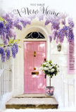 This photograph offers a tender glimpse of a new home moment in Clerkenwell, the kind of scene you might stumble upon wandering from Farringdon Station towards the quieter residential streets near Clerkenwell Green. A pastel pink front door stands at the centre, its paint smooth and matte, radiating a soft warmth that seems to cradle the entrance. Above it, wisteria cascades in generous sweeps of lavender and lilac, each trail of blossom forming a loose canopy that falls around the doorway like draped fabric. The blossoms appear dense yet airy, with tiny petals clustering along elegant stems that sway slightly in an invisible breeze. Whitewashed walls to either side create a calm, bright frame, while a coordinating blush-toned shutter adds another brushstroke of gentle colour. Just in front of the door, set carefully upon a stone step worn by many arrivals and departures, sits a grey metal bucket brimming with roses. The roses are white and soft cream, full-headed and plush, accompanied by a few stems of muted green foliage that add depth without disturbing the serene palette. Around the base of the bucket, a pink ribbon is tied in a simple, graceful bow, its satin sheen catching the light. The whole arrangement feels like a quiet housewarming gift left by a thoughtful friend, perhaps delivered earlier in the day by a local florist who understands how flowers can ease the transition into a new space. The atmosphere is gentle, hopeful, and intimate, perfectly suited to those first days when a new house in Clerkenwell slowly begins to feel like home.